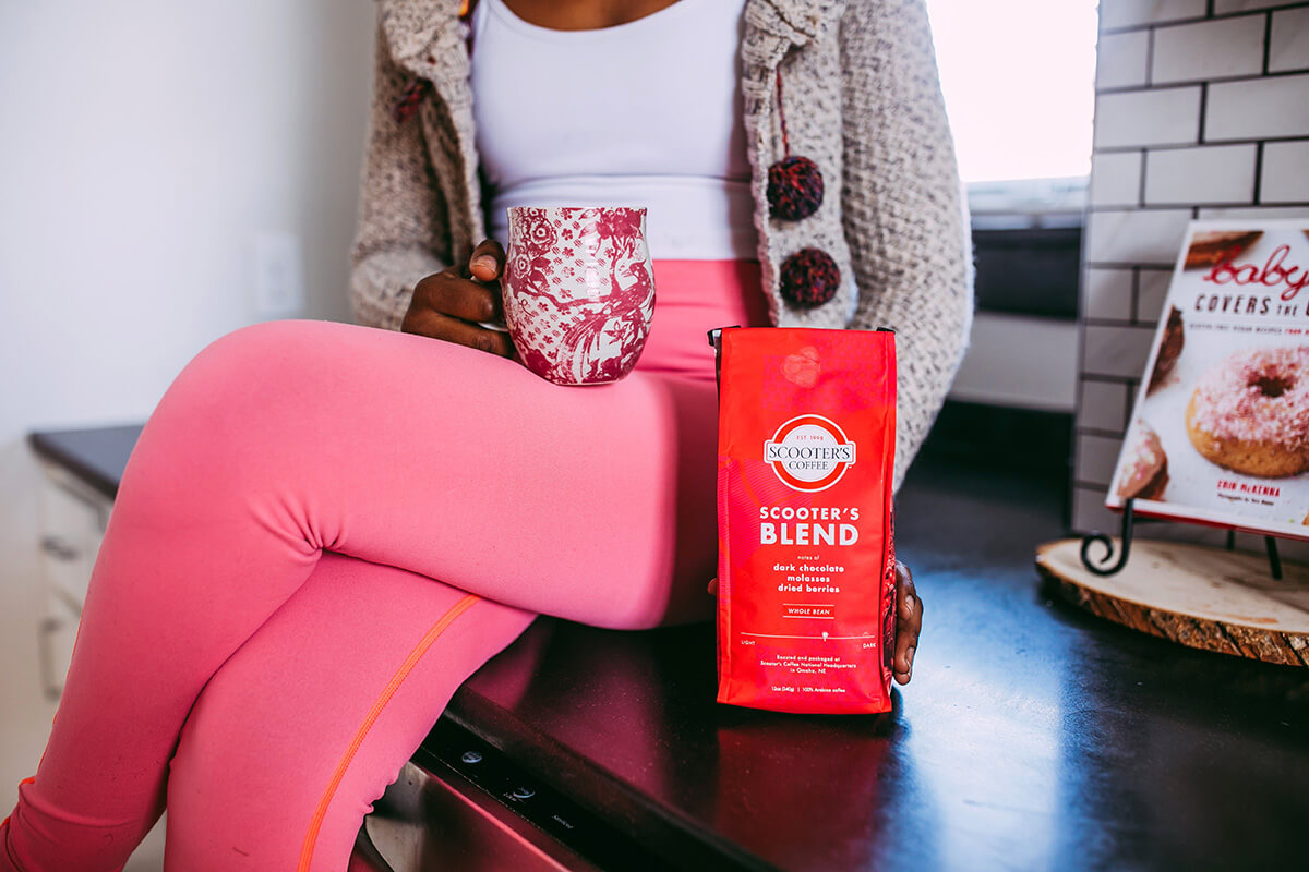 Woman holding cup of coffee and red bag of Scooter's Blend coffee