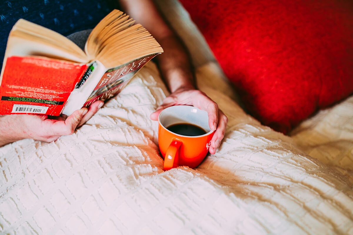 Person sitting in bed with coffee reading a book