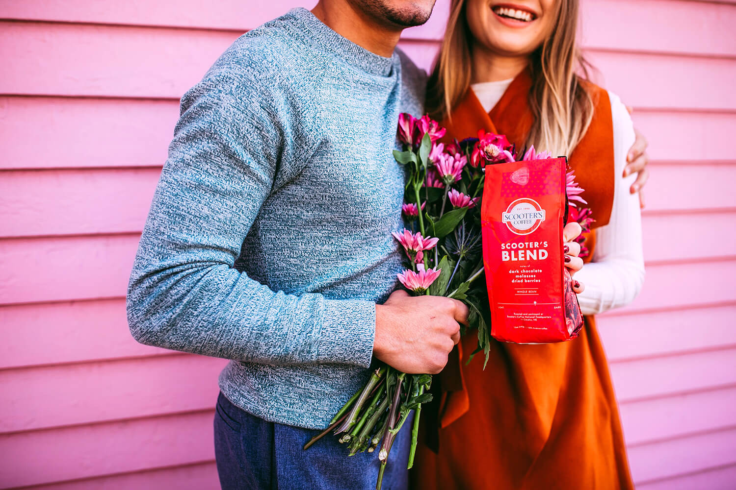 Man holding flowers next to woman holding red Scooter's Coffee bagged coffee