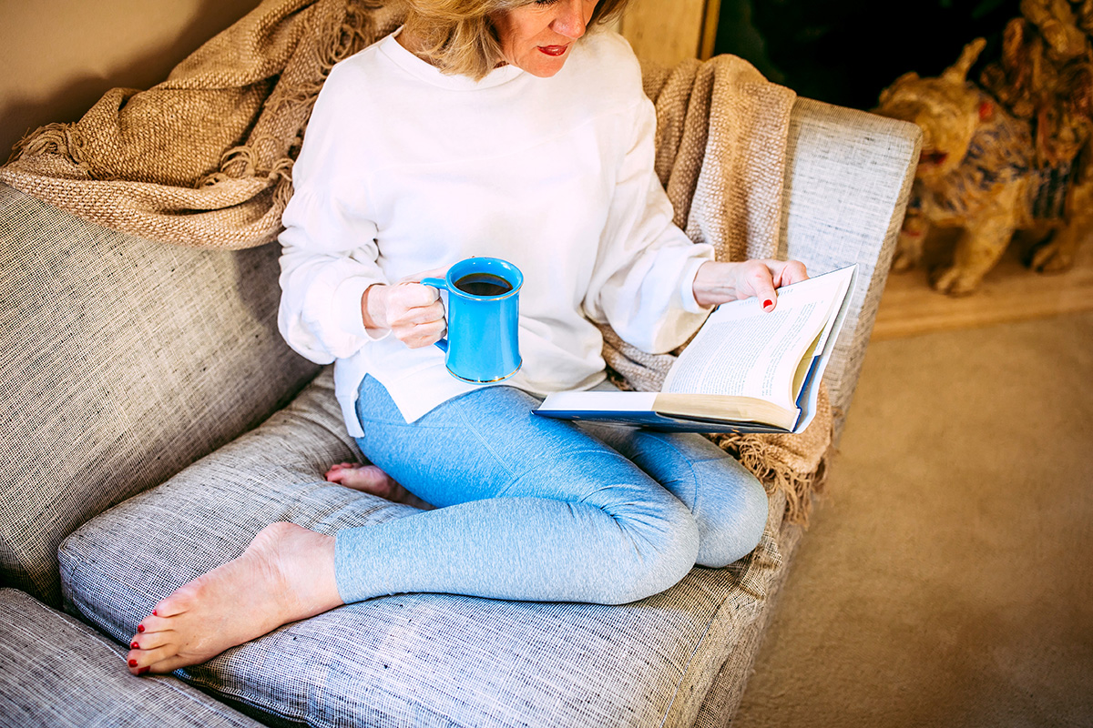 Woman on couch reading book with coffee