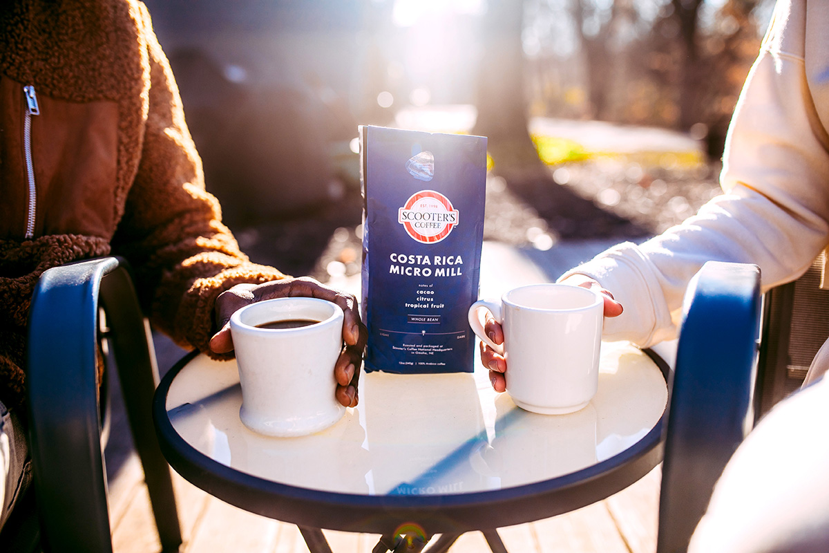 Two people sitting at table with coffee cups and bag of Costa Rica Micro Mill