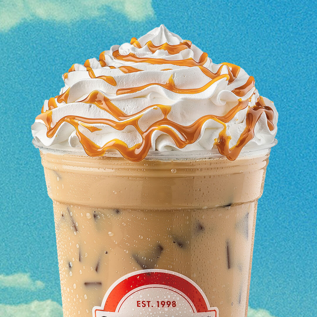 Iced coffee topped with whipped cream and caramel drizzle on blue background